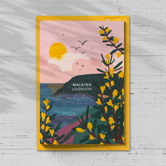 A Walking Logbook with a scenic design of a sunset over water and yellow flowers from the Pencil Me In stationery shop.