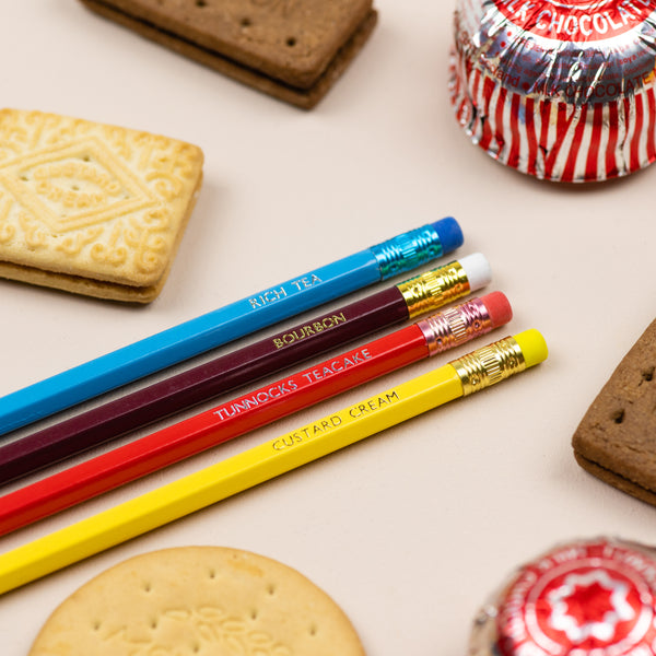 A foil printed set of biscuit pencils in a gift box from the Pencil Me In stationery shop reading ‘RICH TEA, BOURBON, TUNNOCKS TEACAKE and CUSTARD CREAM’.